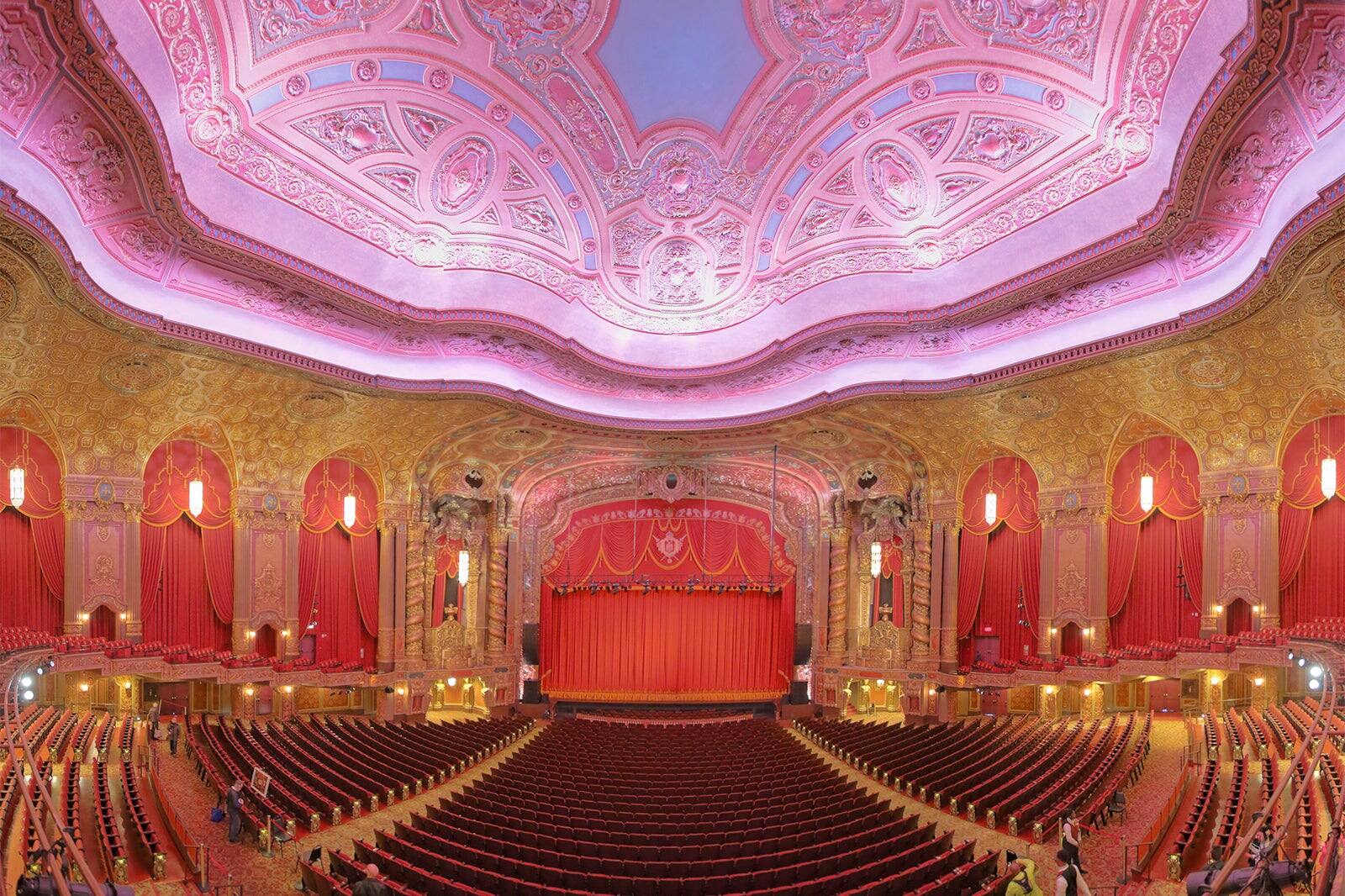 Broadway shows in NYC: Ornate Broadway theatre interior with luxurious red velvet seats, grand chandeliers, and an intricately decorated pink and gold ceiling in New York City