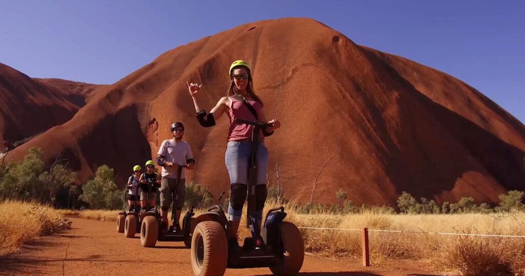 Uluru travel guide: Tourists riding Segways along the Uluru Base Walk in Australia’s Red Centre, enjoying an eco-friendly guided tour with Uluru’s sandstone monolith in the background