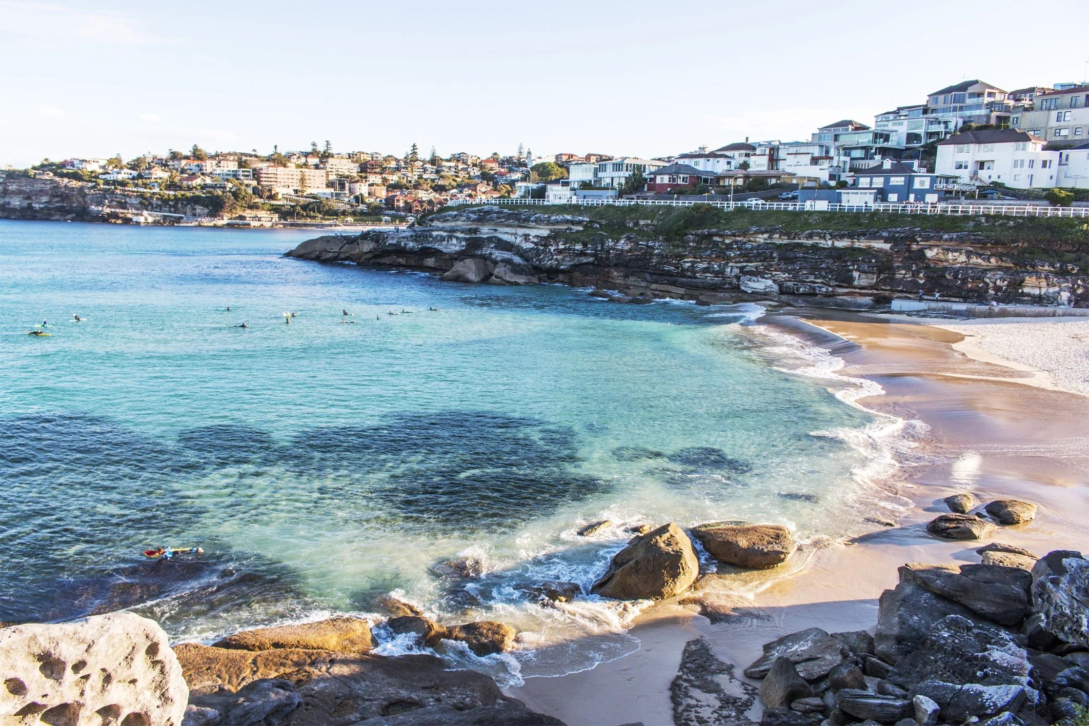 Turquoise waters and rocky shoreline at Tamarama Beach near Bondi in Sydney, Australia, with surfers and coastal homes in the background"
