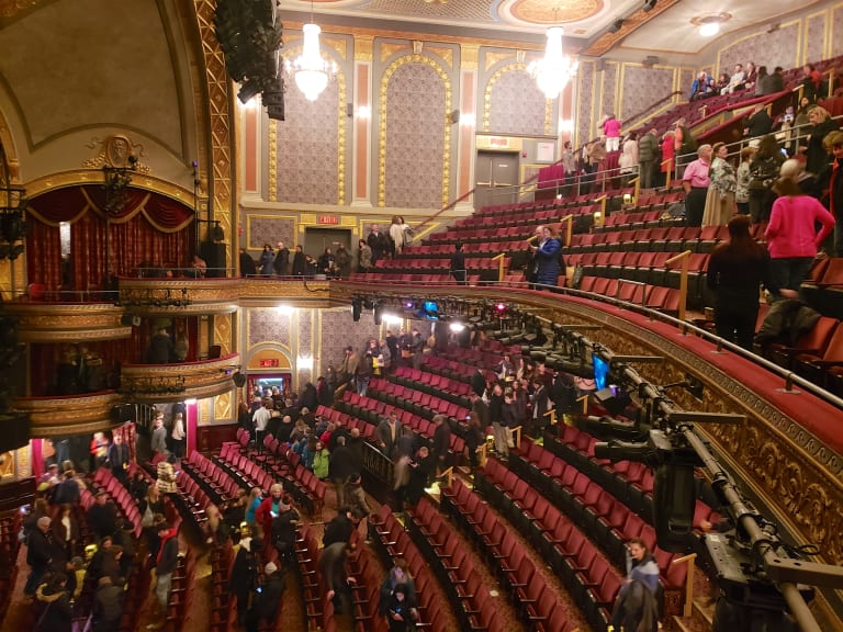 Broadway shows in NYC: Interior view of a historic Broadway theatre with ornate balconies, chandelier lighting, and red velvet seating as audience exits after a show