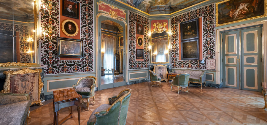 "Lavishly decorated Rococo-style interior room in the Chateau de Versailles, featuring antique furniture, parquet flooring, floral wallpaper, and gilded portraits"