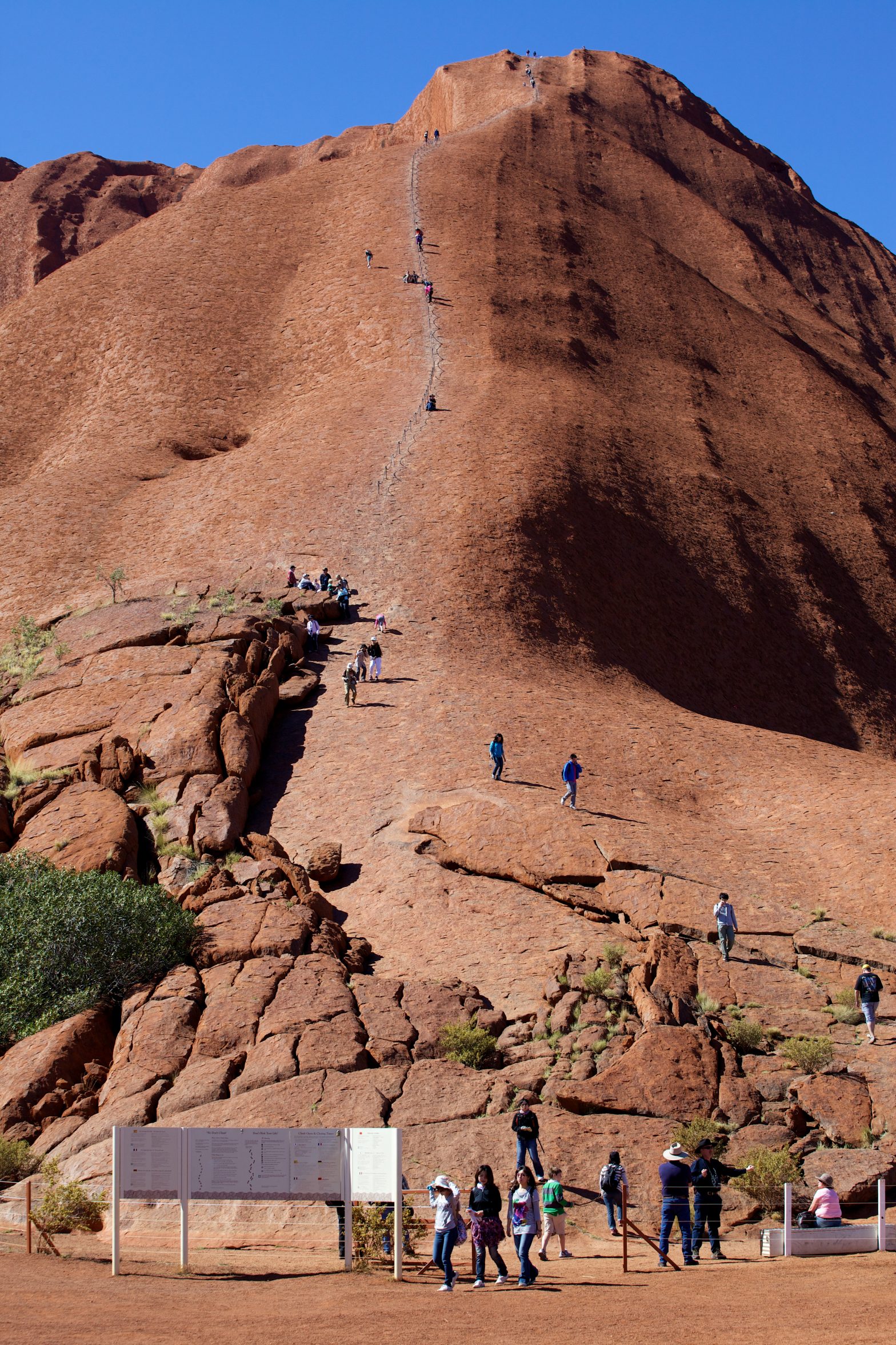 Tourists climbing Uluru (Ayers Rock) before the 2019 cultural ban, showcasing the steep sandstone path and iconic red landscape under a clear blue sky in Australia’s Red Centre