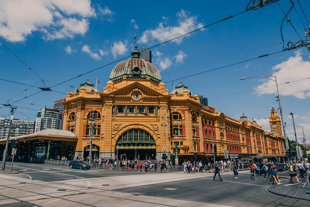 Flinders Street Station in Melbourne, Australia, with its iconic yellow facade and dome, bustling with tourists and city traffic on a sunny day