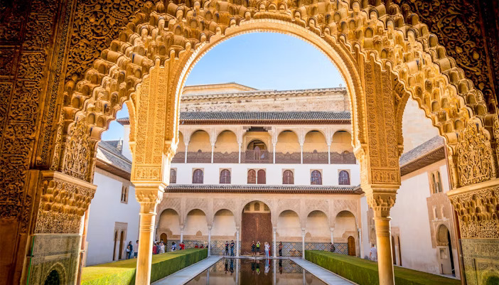 "View through an ornate Islamic arch into the Court of the Myrtles at the Alhambra in Granada, Spain, with symmetrical arches, reflecting pool, and Nasrid Palace architecture"