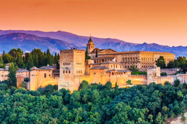 "Panoramic view of the Alhambra palace and fortress complex in Granada, Spain, with the Sierra Nevada mountains in the background at sunset"