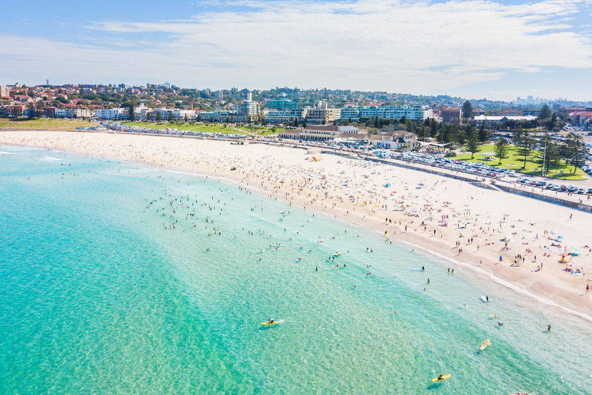 Aerial view of Bondi Beach in Sydney, Australia, with clear turquoise water, surfers, and sunbathers on the sandy shoreline
