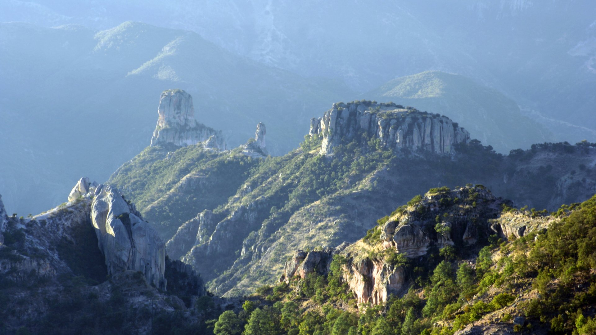 "Dramatic rock formations and rugged green mountains of Copper Canyon in Chihuahua, Mexico, under soft morning light"