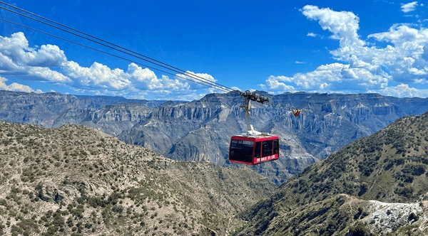 "Red aerial tramway crossing over Copper Canyon in Chihuahua, Mexico, surrounded by lush green mountains and dramatic cliffs"