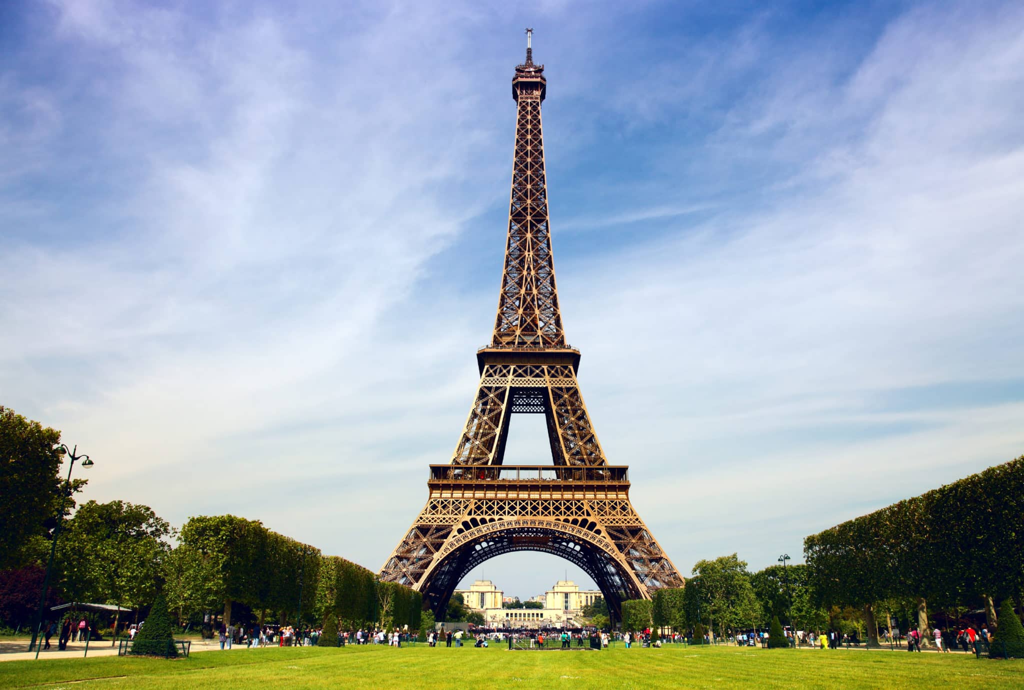 The Eiffel Tower in Paris, France, viewed from the Champ de Mars on a clear day with tourists gathering around the landmark