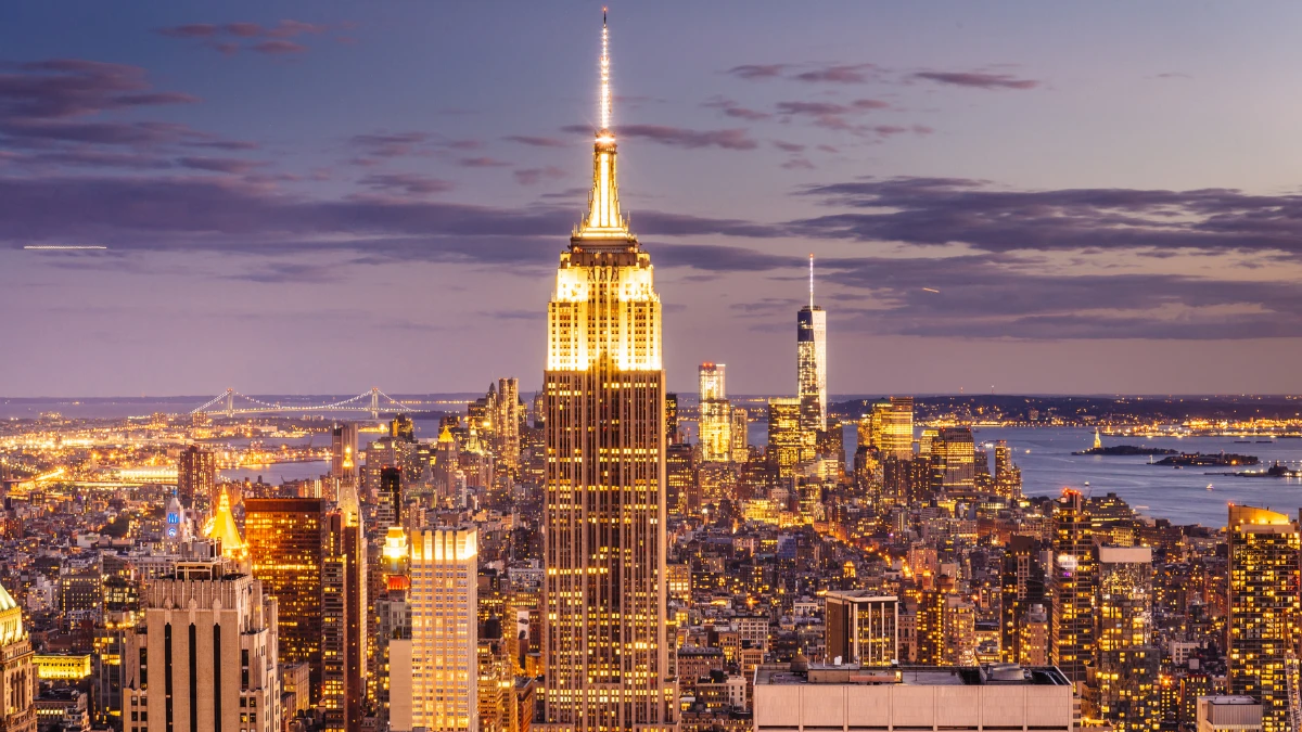 Empire State Building illuminated at dusk with panoramic view of New York City skyline and sparkling city lights in the background.