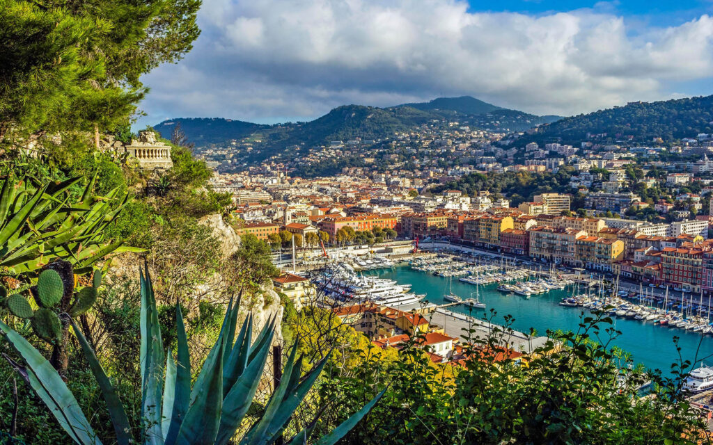 Panoramic view of Nice, France with colorful buildings, luxury yachts in the marina, and surrounding hills seen from Castle Hill on the French Riviera