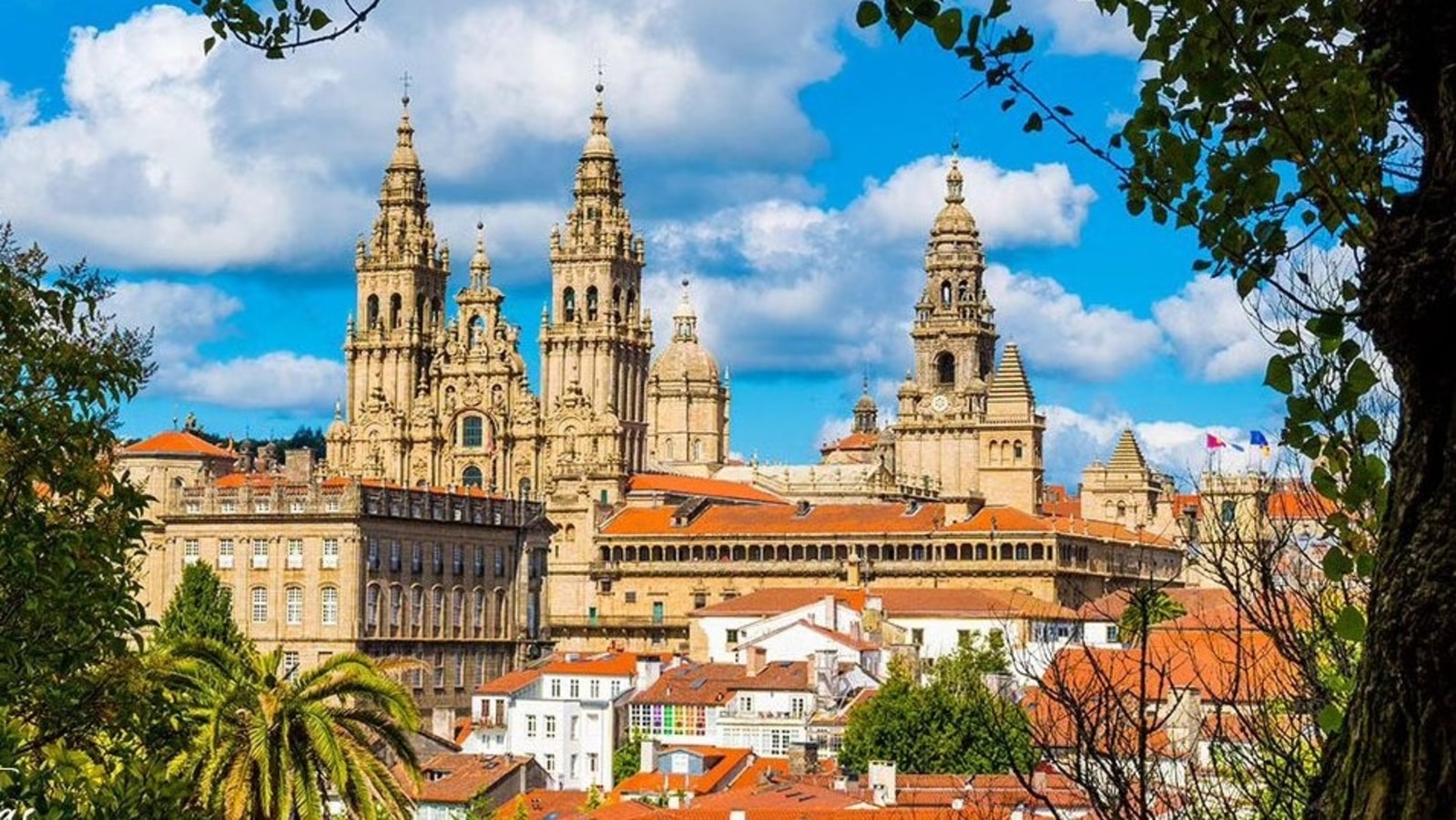 "Panoramic view of the Cathedral of Santiago de Compostela in Galicia, Spain, with its iconic Baroque towers rising above the old town rooftops under a blue sky"