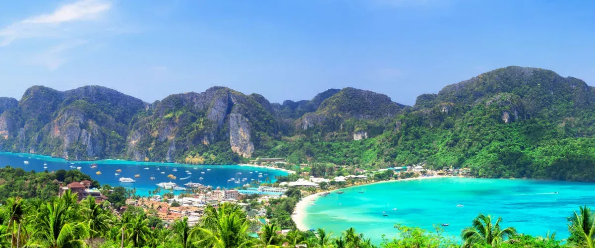 "Panoramic view of Phi Phi Islands in Thailand with turquoise bays, lush green mountains, sandy beaches, and boats anchored in the clear Andaman Sea "