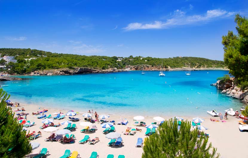 "Sunny day at Cala Nova beach in Ibiza, Spain, with turquoise water, white sand, colorful umbrellas, and sunbathers enjoying the Mediterranean coast"