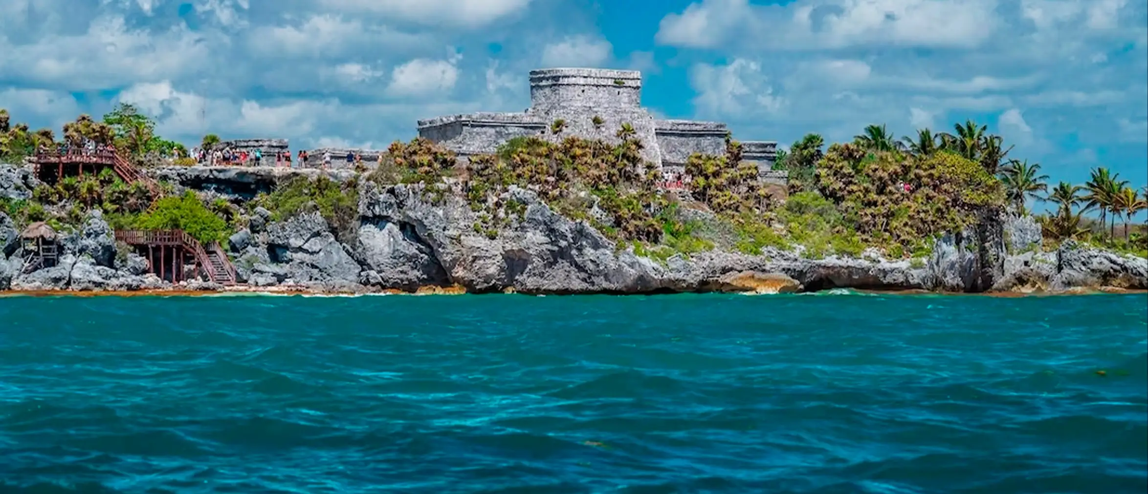"Ancient Mayan ruins of Tulum perched on a cliff above turquoise Caribbean waters under a bright blue sky in Mexico"