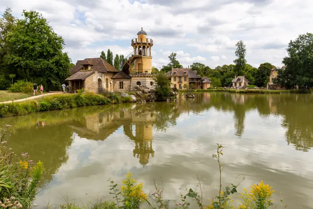 Chateau de Versailles travel guide: Marie Antoinette’s rustic hamlet and tower reflecting in a peaceful lake at the Chateau de Versailles estate in France