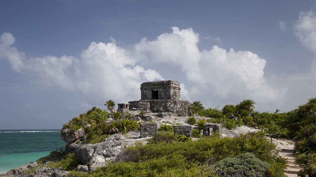 "Ancient Mayan temple on a cliff overlooking the Caribbean Sea at Tulum Ruins in Riviera Maya, Mexico, under a cloudy sky"