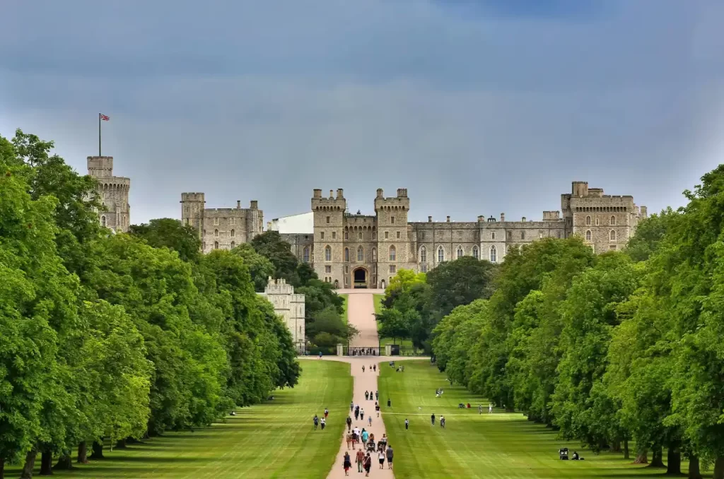 Royal Palace of Madrid travel guide: "Scenic view of Windsor Castle in England with tourists walking along the Long Walk lined by trees on a cloudy day"