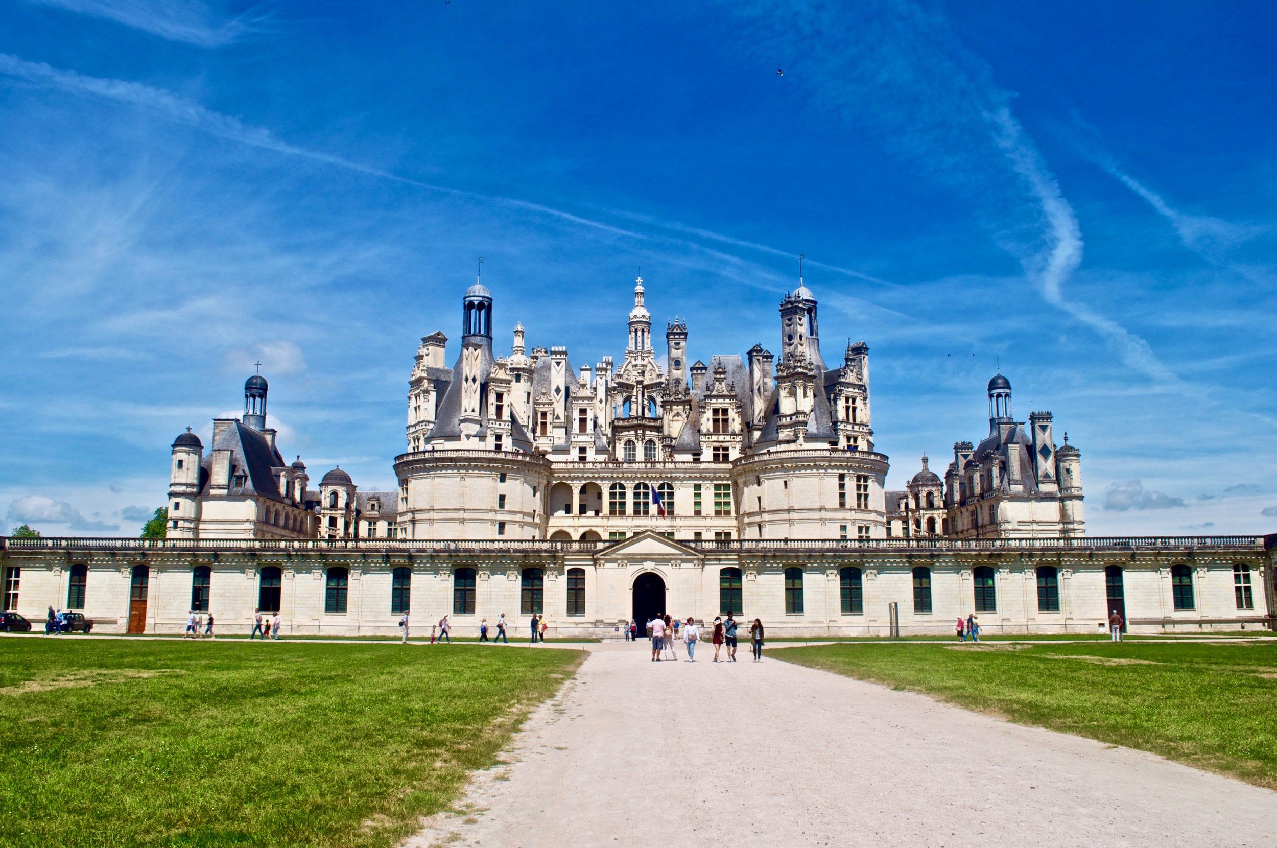 Tourists walking toward Chateau de Chambord under a clear blue sky in the Loire Valley, France, showcasing French Renaissance architecture and cultural heritage