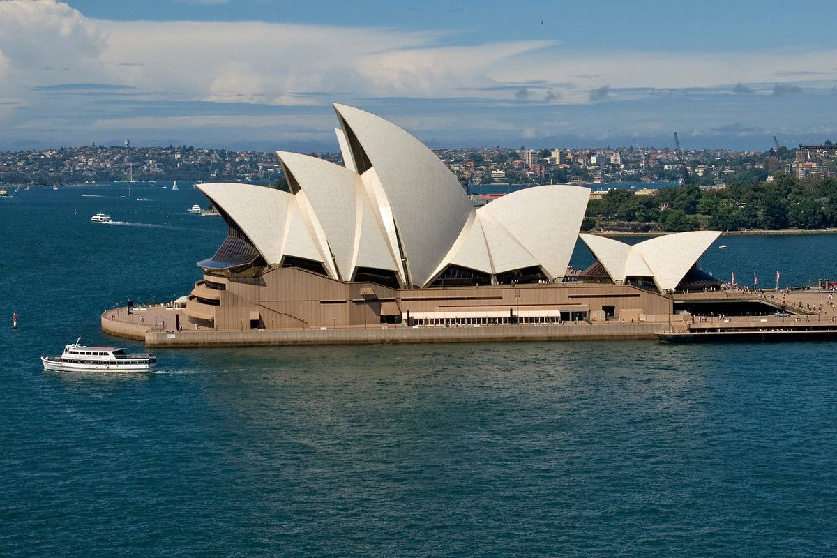 Sydney Opera House with its iconic sail-like architecture viewed from across the harbour on a sunny day, with boats and cityscape in the background