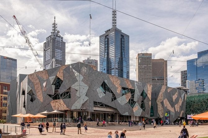 Federation Square in Melbourne, Australia, with modern geometric architecture and people walking in the public square on a partly cloudy day