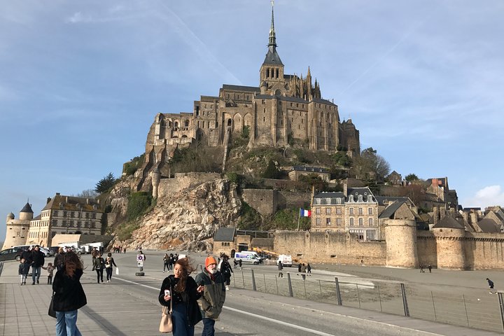 Visitors walking along the bridge to Mont Saint-Michel, a medieval abbey and UNESCO World Heritage site in Normandy, France, on a clear day