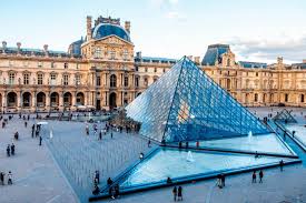 Louvre Museum in Paris with the iconic glass pyramid entrance surrounded by visitors in the main courtyard during the day