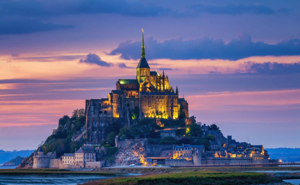 Mont Saint-Michel illuminated at sunset with vibrant purple and pink skies, showcasing the medieval island abbey in Normandy, France