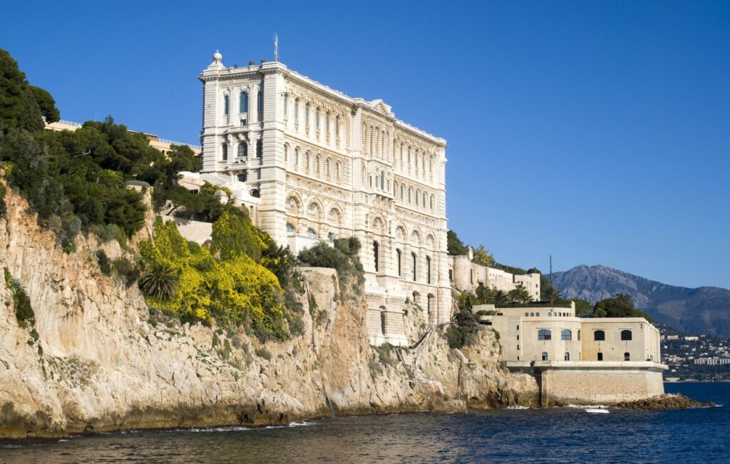 Oceanographic Museum of Monaco perched on a cliff overlooking the Mediterranean Sea, with a clear blue sky and scenic coastal backdrop