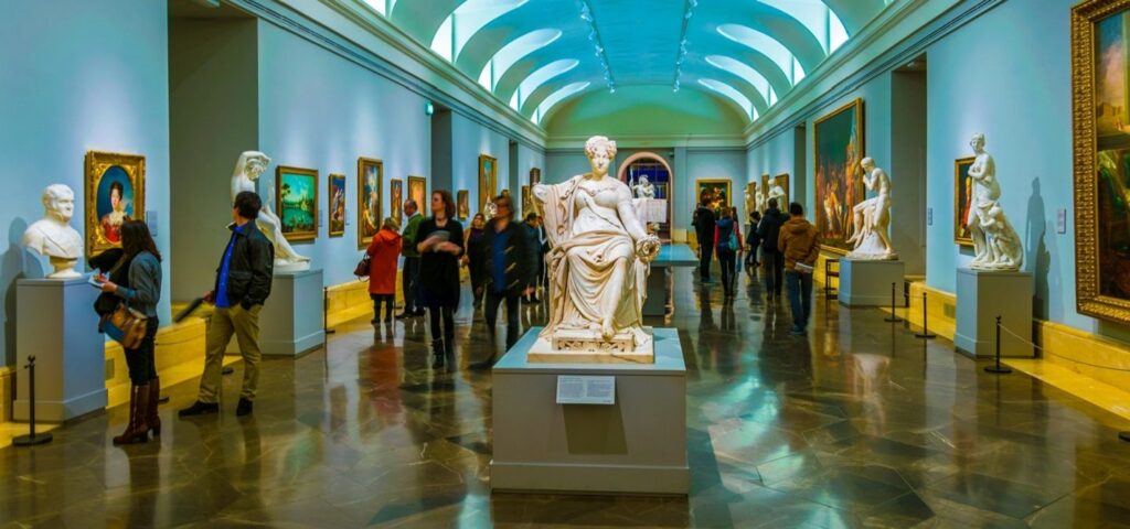 "Visitors exploring classical sculptures and European paintings inside an elegant gallery hall at the Prado Museum in Madrid, Spain"