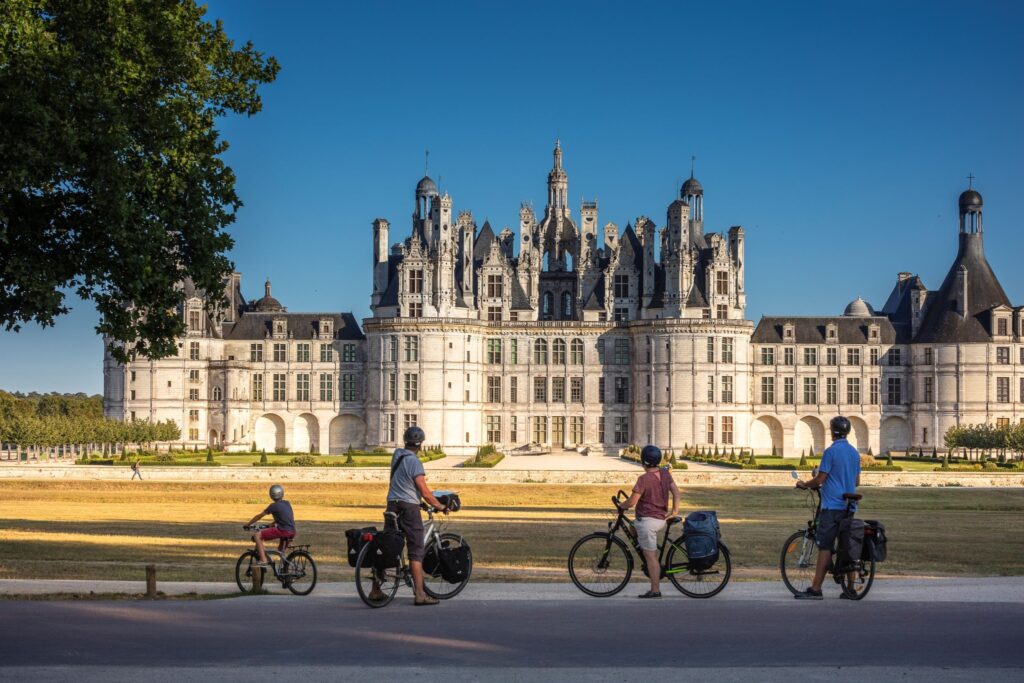 Cyclists admiring Château de Chambord in the Loire Valley, France, on a sunny day, showcasing Renaissance architecture and scenic cycling routes