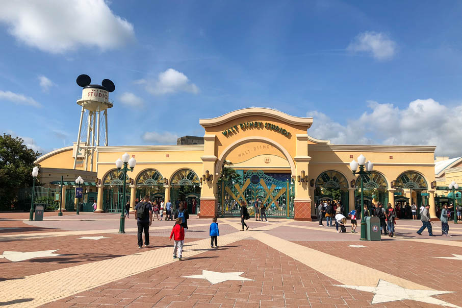"Entrance to Walt Disney Studios Park at Disneyland Paris with visitors walking toward the iconic Mickey Mouse water tower and art deco-style gates under a blue sky"
