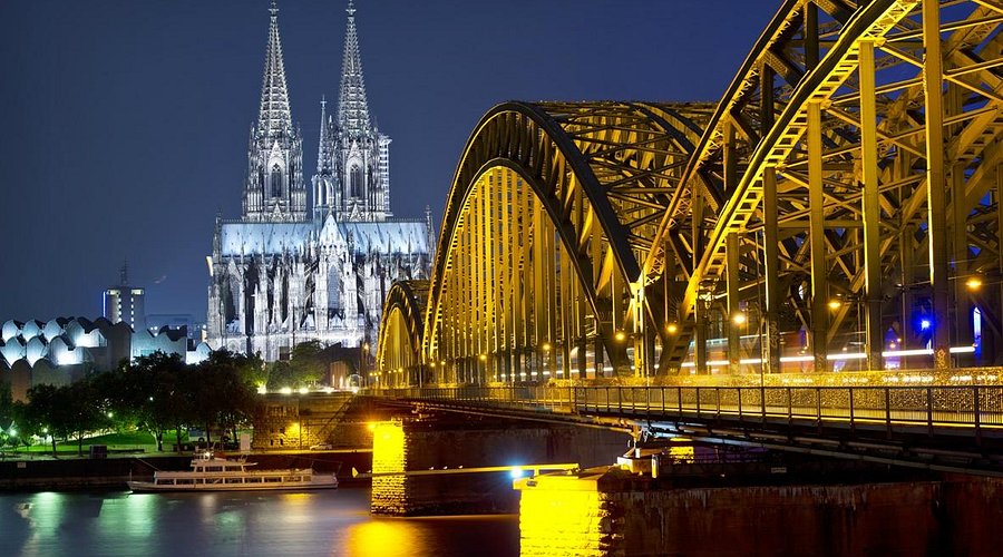 "Cologne Cathedral illuminated at night with the Hohenzollern Bridge crossing the Rhine River in Cologne, Germany"