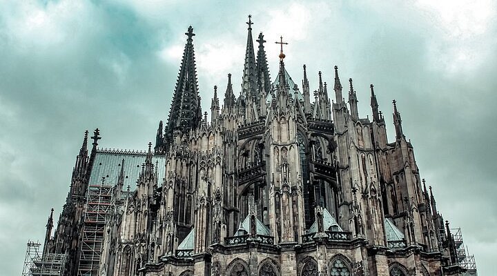 "Detailed view of the Gothic architecture of Cologne Cathedral in Germany, with towering spires and cloudy sky in the background"