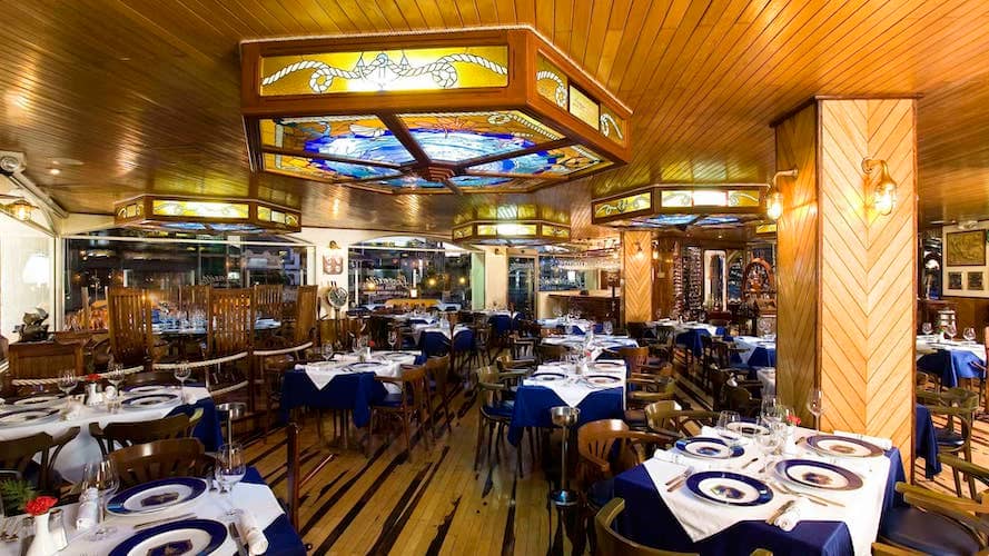 "Elegant seafood restaurant interior in Cancun, Mexico, featuring nautical-themed décor, stained glass ceiling panels, and neatly arranged tables with blue and white settings"