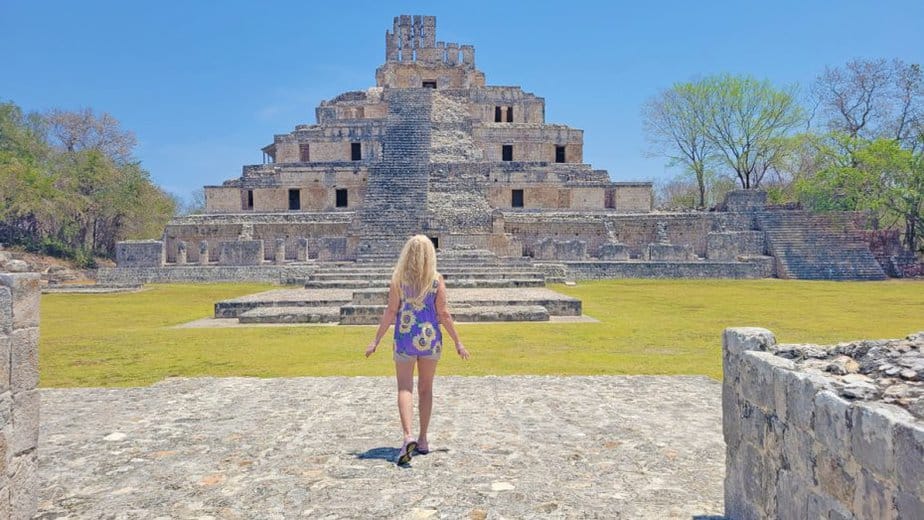 "Woman walking toward the ancient Maya pyramid of Edzná in Campeche, Mexico, under a clear blue sky on a sunny day"