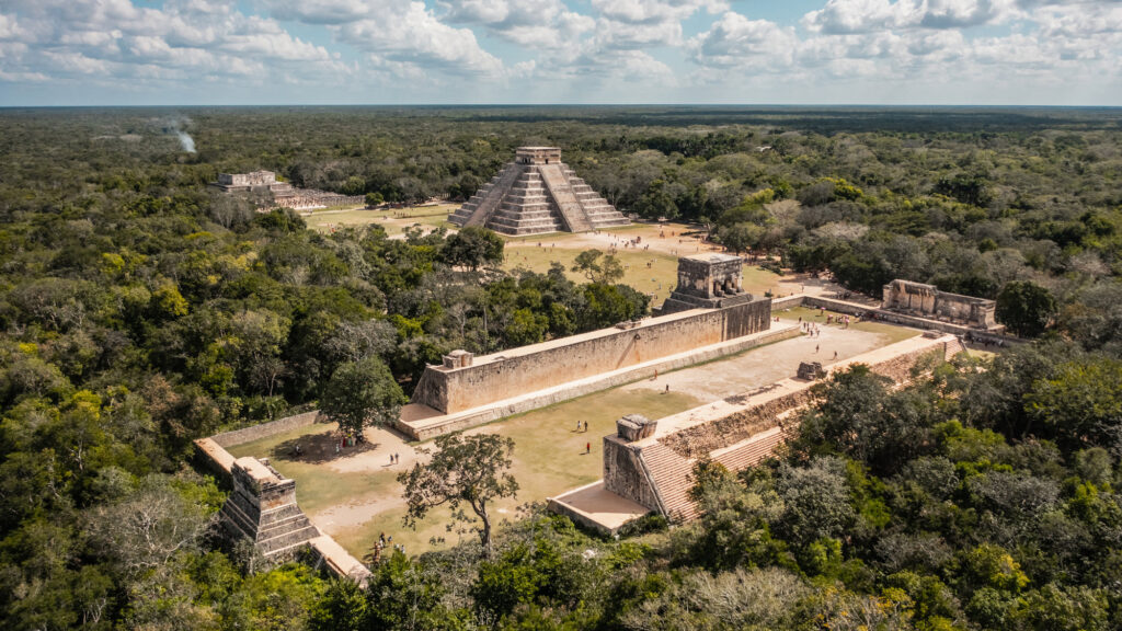"Aerial view of Chichen Itza archaeological site in Mexico featuring El Castillo pyramid, Great Ball Court, and surrounding jungle in the Yucatán Peninsula"