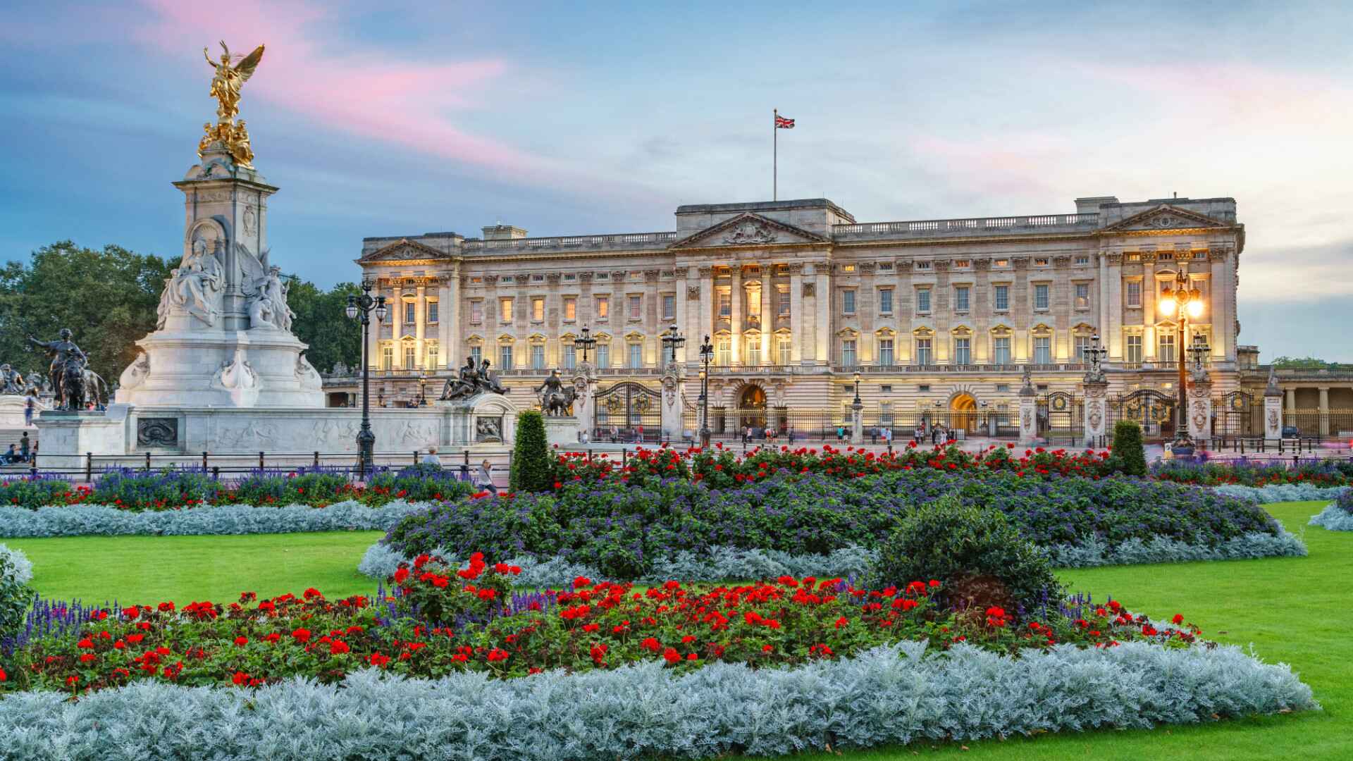 "Buckingham Palace in London with the Victoria Memorial and colorful flower gardens in the foreground during sunset"