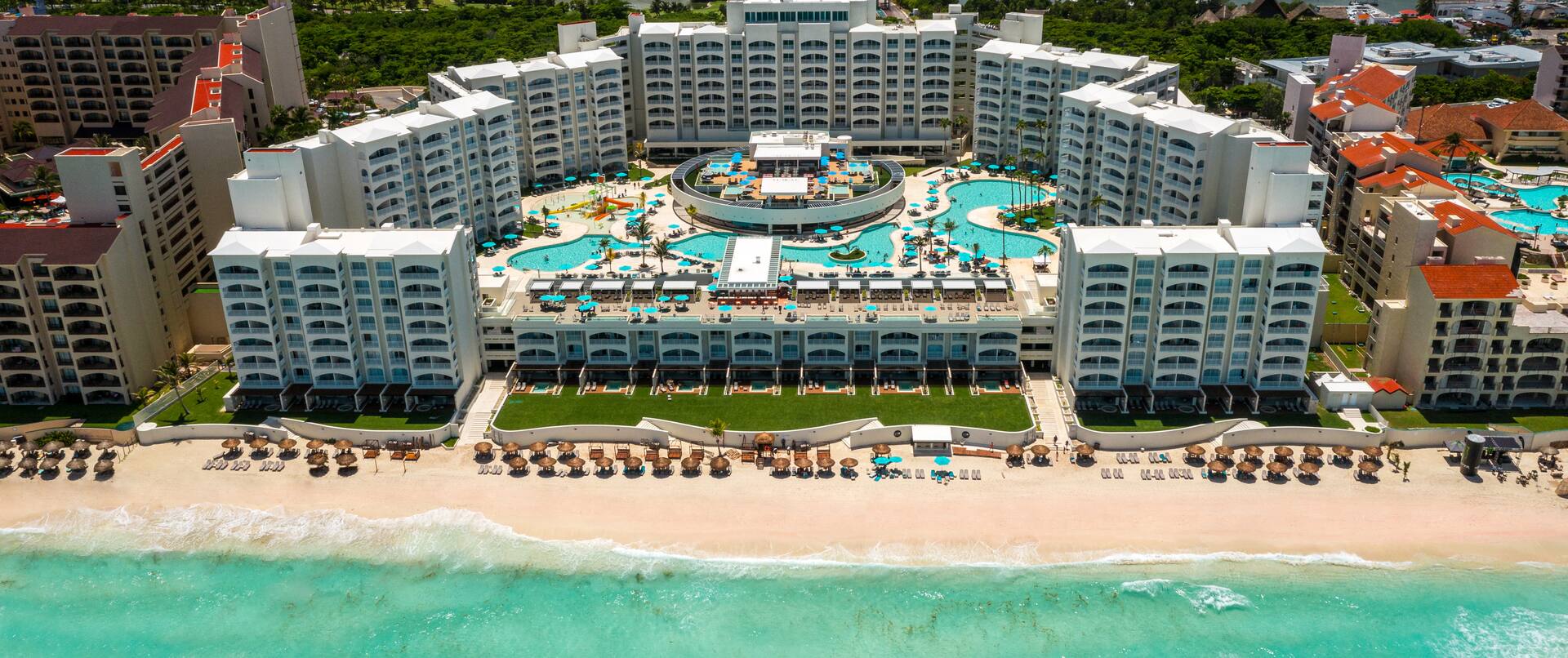 Cancun travel guide : Aerial view of a luxury beachfront resort in Cancun, Mexico, featuring turquoise pools, oceanfront balconies, private cabanas, and white sand beach along the Caribbean Sea"