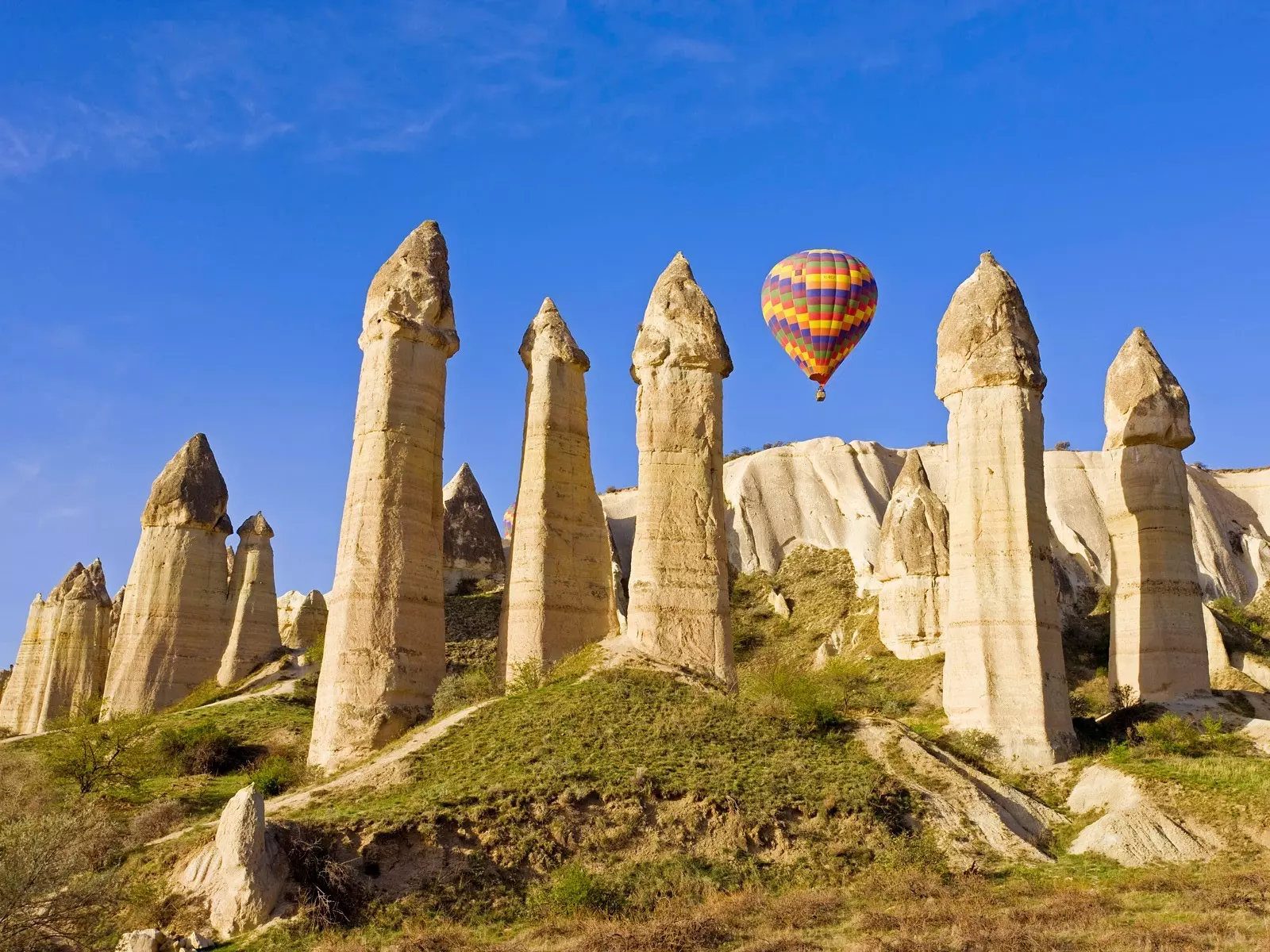 "Hot air balloon floating over the fairy chimneys in Cappadocia, Turkey, under a clear blue sky during sunrise"