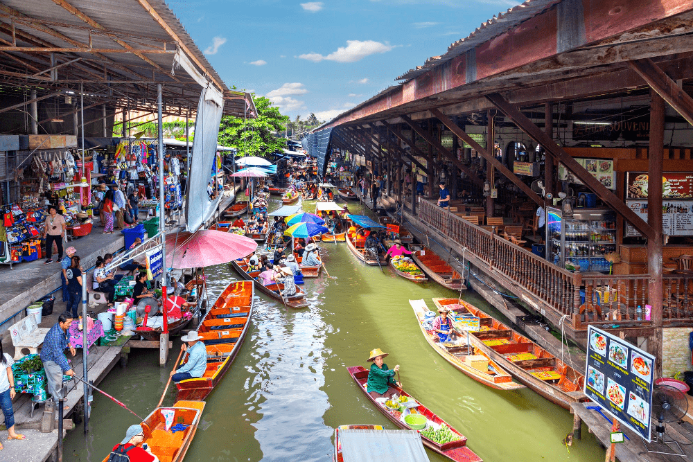Thailand floating markets: "Vendors selling tropical fruits, local food, and souvenirs from colorful wooden boats at the Damnoen Saduak Floating Market in Thailand"