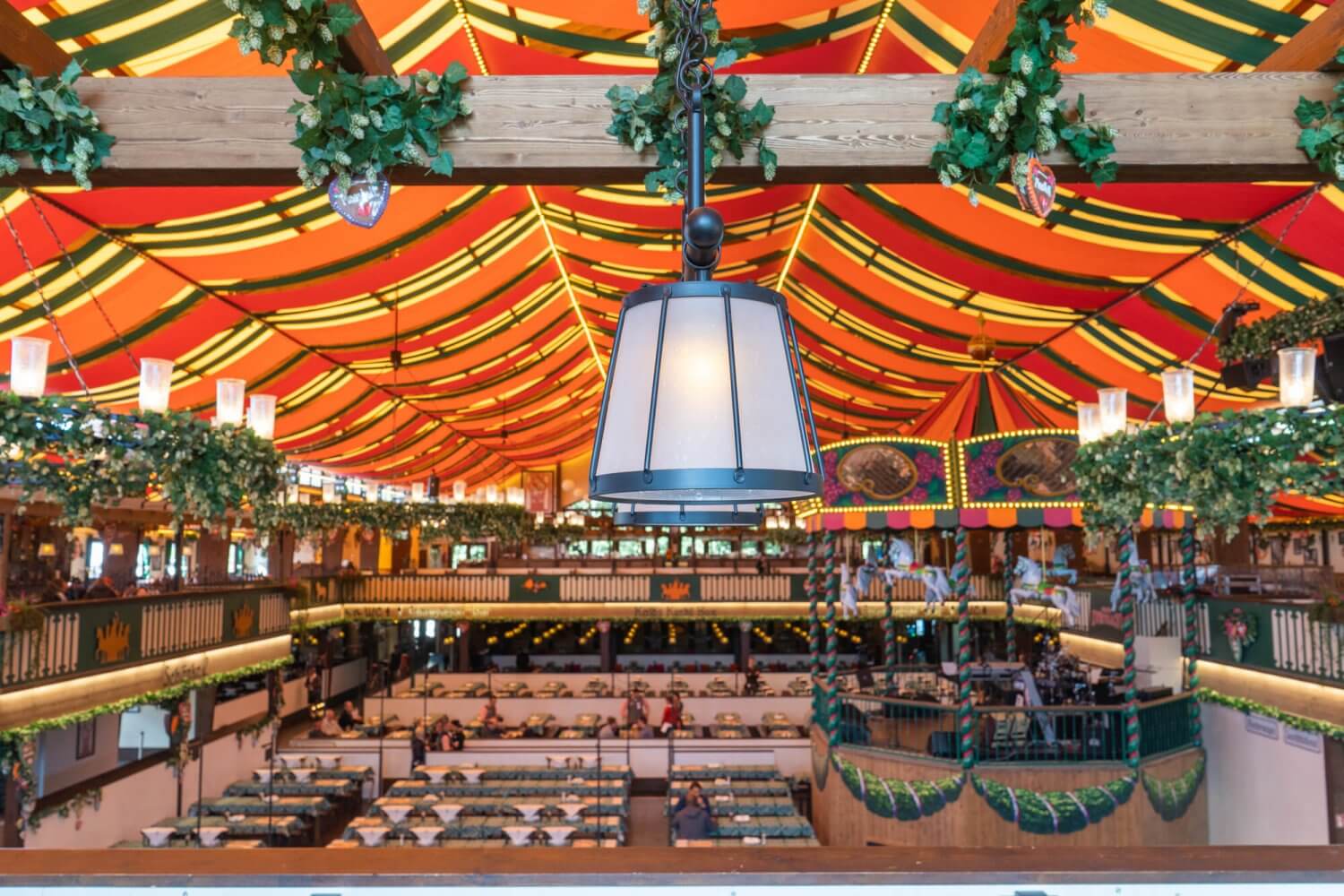 "Interior of a traditional Oktoberfest beer tent in Munich, Germany, featuring colorful striped ceiling, hanging decorations, and long wooden tables prepared for festival guests" Oktoberfest in Munich