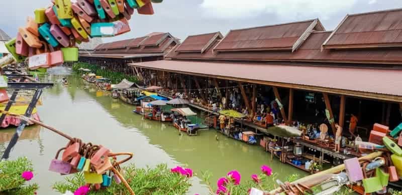"View of Pattaya Floating Market in Thailand with wooden pavilions, boats selling local food, and colorful love locks in the foreground"