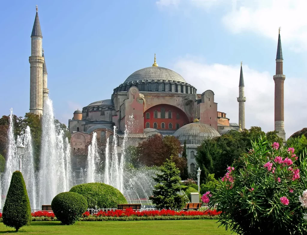 Hagia Sophia, Istanbul's crown jewel: "Hagia Sophia in Istanbul, Turkey, with its grand domes and minarets behind a fountain and garden in Sultanahmet Square on a sunny day"