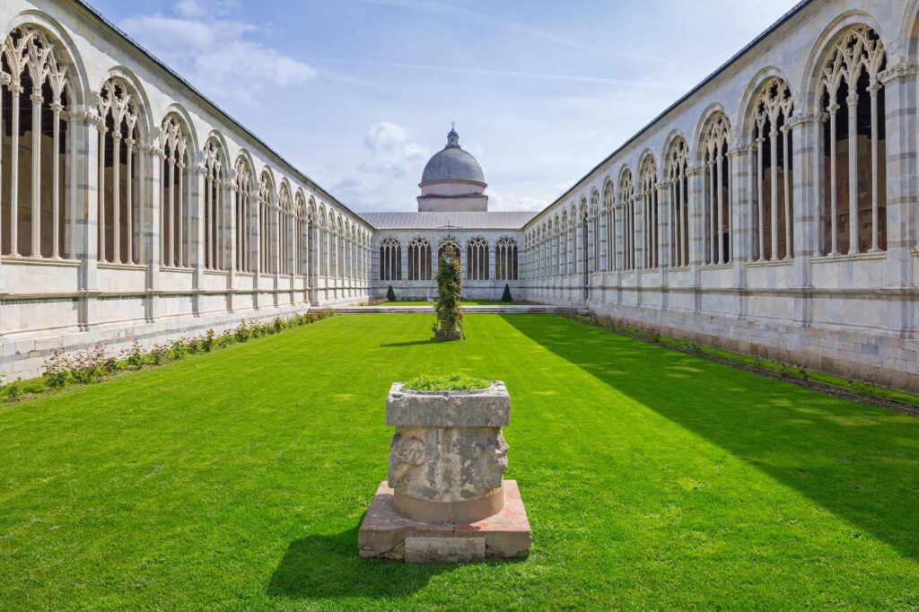 Leaning Tower of Pisa: "The Camposanto Monumentale in Pisa, Italy, featuring its elegant Gothic arches, marble courtyard, and green lawn under a bright blue sky"