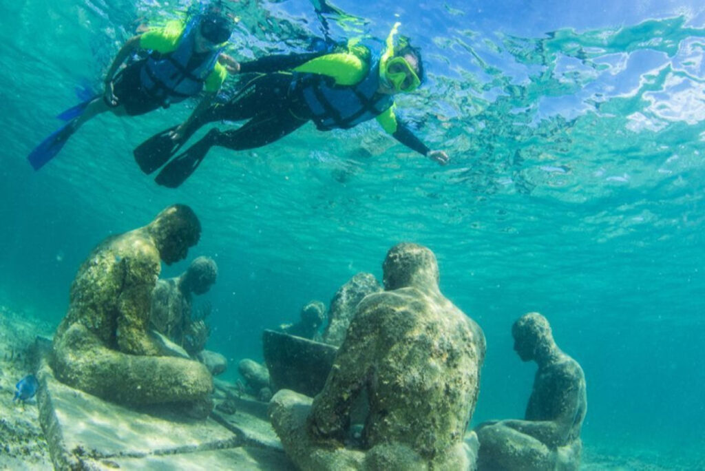 "Snorkelers exploring underwater sculptures at the Cancun Underwater Museum (MUSA) in Mexico, featuring coral-covered statues creating an artificial reef in the Caribbean Sea"