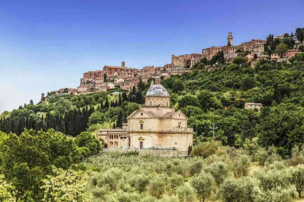 "View of Montepulciano hill town in Tuscany, Italy, with the Church of San Biagio surrounded by lush green vineyards and olive groves under a clear blue sky"
