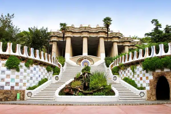 "Main staircase and Hypostyle Hall at Park Güell in Barcelona, Spain, featuring colorful mosaic tiles, lush greenery, and Gaudí’s distinctive architectural design"