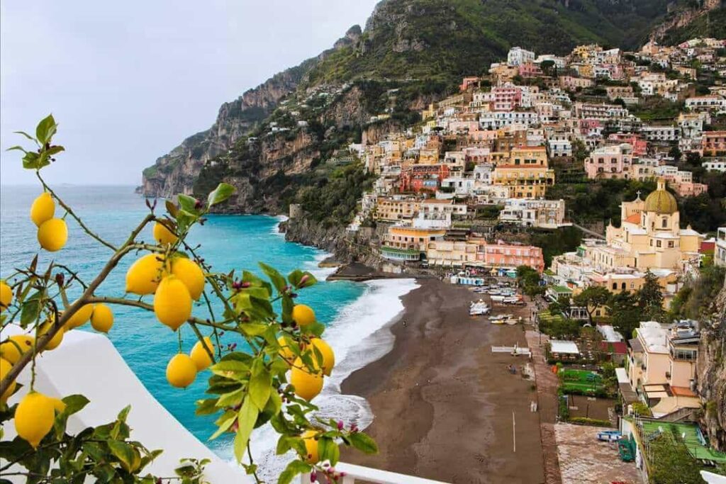 "View of Positano on the Amalfi Coast in Italy with colorful hillside houses, turquoise sea, and lemon trees in the foreground"