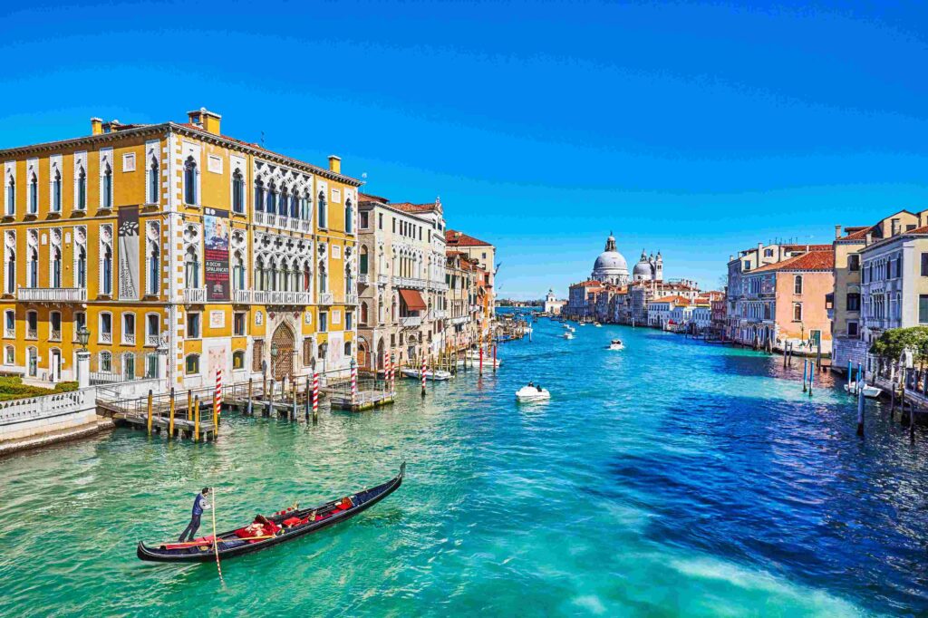 "Gondola gliding along the Grand Canal in Venice, Italy, surrounded by colorful historic buildings and clear blue water under a bright sunny sky"